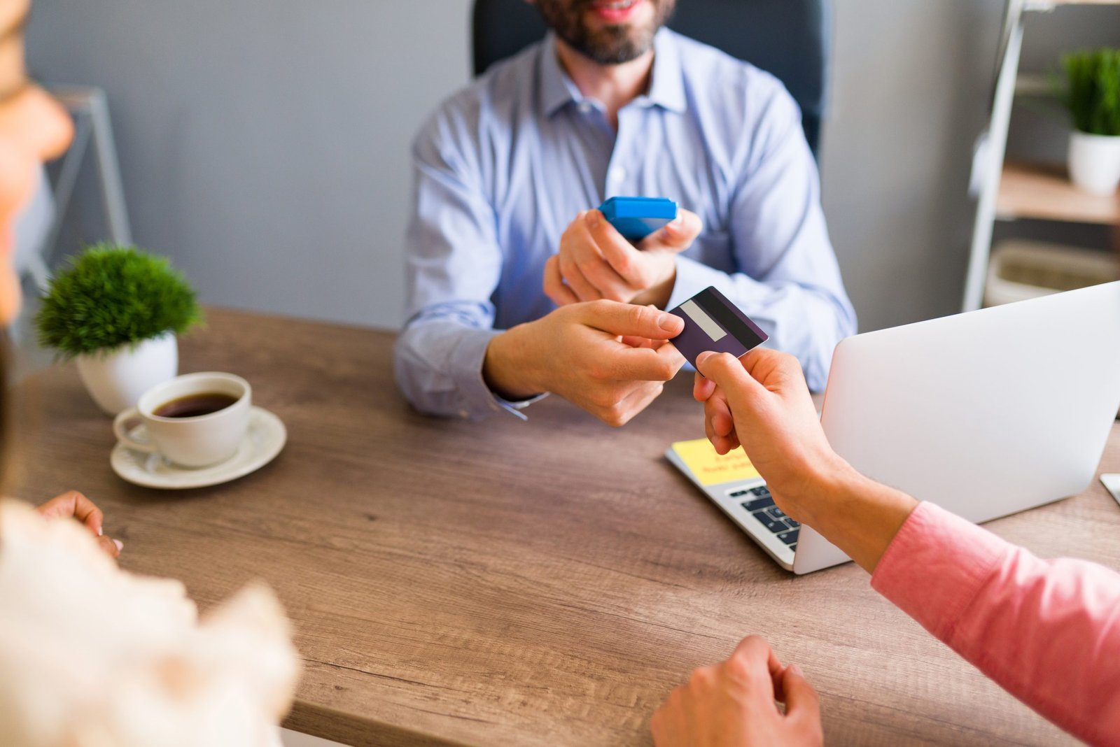 Close up of an hispanic man giving his credit card to a sales representative at the travel agency to pay for his business trip or holiday vacation